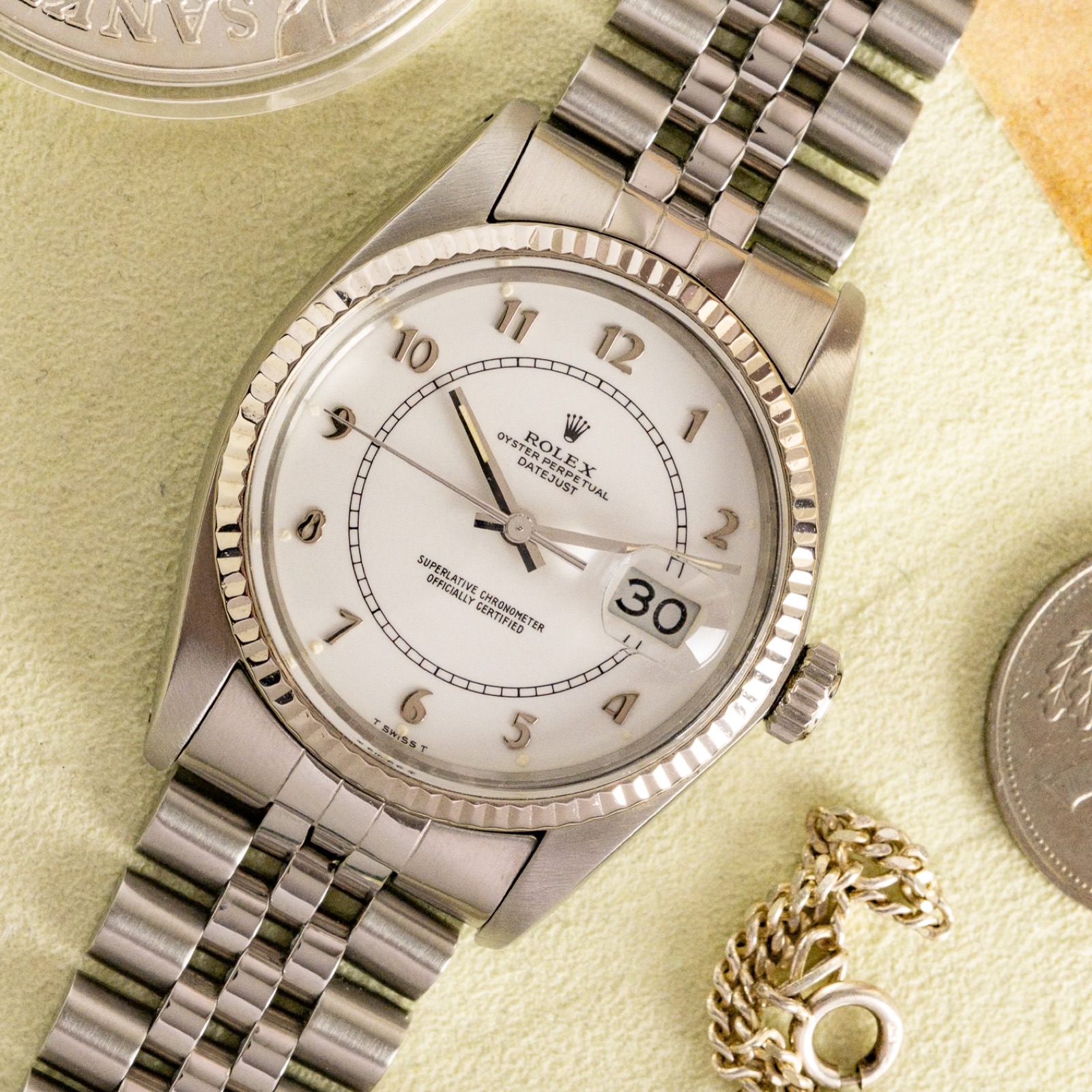 Eine Rolex Datejust von oben, auf hellem Tuch zwischen alten Münzen und Papieren